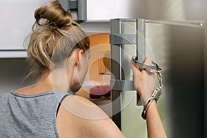 Food addiction and gluttony concept - woman cuffed to the handle looking inside the fridge photo