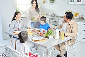 Food for all. Happy latin family having dinner together at home. Cheerful woman smiling while serving salad for her