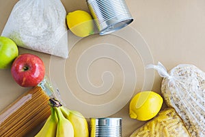 Food assistance, donation. Rice, pasta, oatmeal, apples, canned food, lemons lie on a brown background with place for text