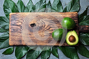 Food background with fresh avocado, avocado tree leaves and wooden cutting board. Harvest concept, Guacamole ingredients. Healthy