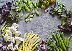 Food background. Fresh garden vegetables on grey background, top view. Cauliflower, beans, peas, chard, fava beans - organic veggi