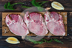 Food background of fresh raw meat of pork chop cutlet steak on wooden board with lemon, green pepper, thyme andv black pepper