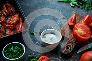 Food background: fresh ripe tomatoes, wooden Board, fresh herbs and spices on a dark background.