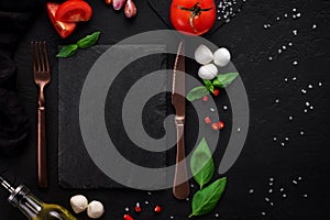 Food background for Italian cuisine. Cooking ingredients for caprese salad with fork and knife around blank slate for recipes