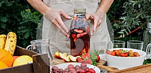 Food banner. Glass bottle with refreshing homemade lemonade or sangria punch with citrus fruits and organic berries. Woman hands