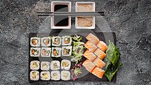 Food banner: set of different rolls on a black stone cutting board. Rolls with salmon, vegetables sushi maki rolls and fresh salad