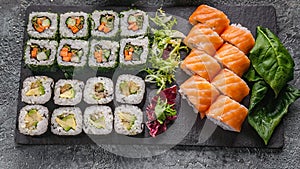 Food banner: set of different rolls on a black stone cutting board. Rolls with salmon, vegetables sushi maki rolls and fresh salad