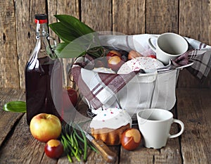 Food basket with a bottle of homemade wine and Easter cakes with eggs on a wooden rustic background.Preparing for a picnic