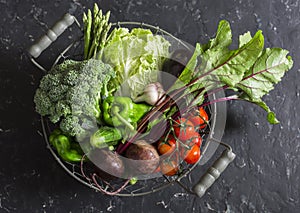 Food basket with fresh garden vegetables - beets, broccoli, eggplant, asparagus, peppers, tomatoes, cabbage on a dark table