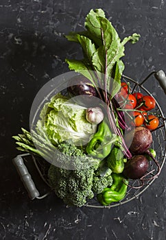 Food basket with fresh garden vegetables - beets, broccoli, eggplant, asparagus, peppers, tomatoes, cabbage on a dark table