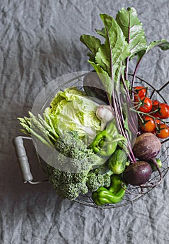 Food basket with fresh organic garden vegetables - beets, broccoli, eggplant, asparagus, peppers, tomatoes, cabbage on a grey tabl