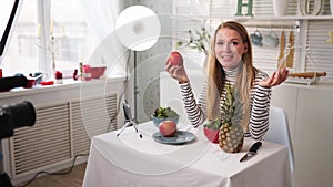 Food blogger cooking fresh vegan salad of fruits in kitchen studio, filming tutorial on camera for video channel. Female