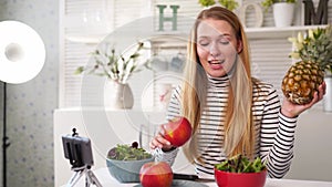 Food blogger cooking fresh vegan salad of fruits in kitchen studio, filming tutorial on camera for video channel. Female