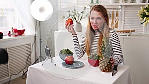 Food blogger cooking fresh vegan salad of fruits in kitchen studio, filming tutorial on camera for video channel. Female