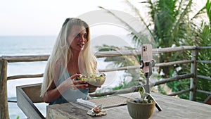 Food blogger woman films video about green salad bowl, dieting for fit skinny body at cafe, sea view. Travel influencer