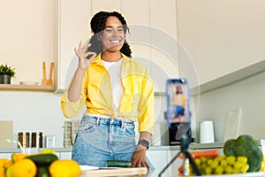 Food blogging. Excited black woman shooting on cellphone in kitchen, cooking and recording video, gesturing ok