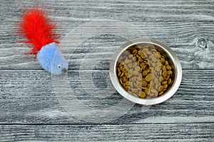 Food for cat in bowl and toy mause on wooden backround. Top view. Close-up