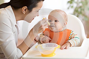 Food, child and parenthood concept - mom with puree and spoon feeding baby at home photo