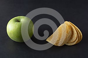 Food choise concept. Potatoe chips or green apple for snack. Top view, black background