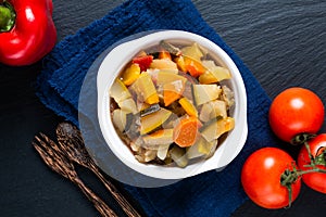 Food concept Homemade French organic Ratatouille in white bake ceramic bowl on blask slate stone board