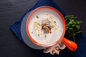 Food concept organic mushroom cream soup in orange ceramic handle bowl on black slate stone with copy space