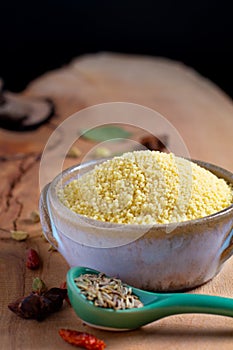 Food concept raw Couscous in brown ceramic bolw and spices on wooden board background