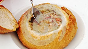 Food concept - Spoon recruit soup. Pouring polish traditional soup called zur or white borscht into bread bowl.