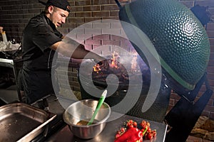 Food concept. Young chef in uniform holds hands on a grill stove. Flames erupt from under on barbecue oven