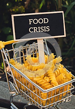 FOOD CRISIS text on Blackboard label Shopping trolley cart Filled With Pasta on agriculture background. Food and