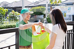 Food Deliver Asian man in green uniform give fruit and vegetable to receiver customer front house