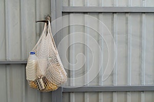 Food delivery. A cotton mesh bag for products with cereals, vegetable oil and milk hangs on a fence. Zero waste, no plastic