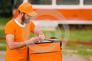 Food delivery man in orange uniform opens a food delivery bag.