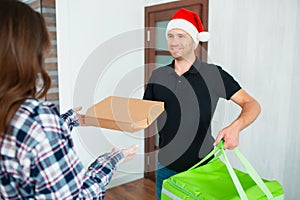 Food delivery man in santa hat. brought the order to the house of a young woman. Merry christmas and happy new year.