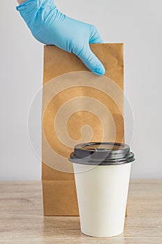 Food delivery during. Mockup of delivery service. female hand in medical gloves holding empty blank craft paper backage next to