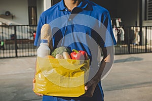 Food delivery service man in blue uniform holding fresh food set bag waiting for customer