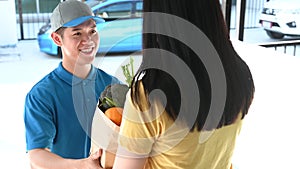 Food delivery service man in blue uniform. Thai deliveryman holding fresh food for young woman.
