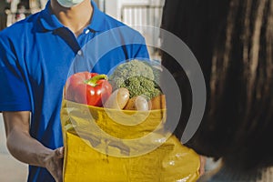 Food delivery service man in blue uniform wearing protection face mask holding fresh food set bag to customer