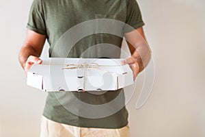 Food delivery service. A man holding a box of pizza on a white background. Close up