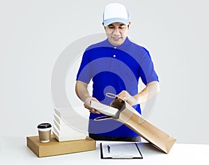 Food delivery service or order food online. Man putting in takeout food container into paper bag with coffee cup in holder and pa