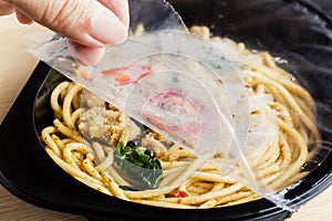Food Delivery service: Woman hands holding open cling wrap and take out food in plastic boxes on wood background. concept online