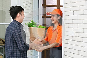 Food delivery service woman in orange uniform handing fresh food to recipient and young man customer receiving order from courier