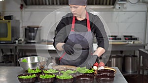 Food delivery or takeaway. Young woman chef in special clothes puts lettuce leaves into disposable lunch boxes.