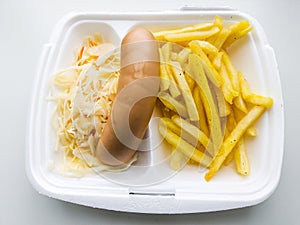 Food in disposable lunch box. French fries, sausage, cabbage and carrot salad