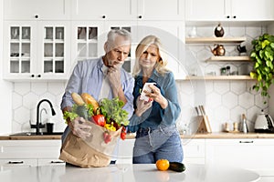 Food Expenses. Stressed Senior Couple In Kitchen Checking Bills After Grocery Shopping