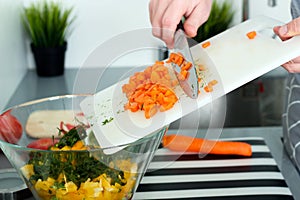 Food, family, cooking and people concept - Man chopping a carrot on cutting board with knife in kitchen