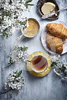 Food flatlay on table with morning tea, flowers, honey, butter and croissants