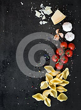 Food frame. Pasta ingredients. Cherry-tomatoes, pasta, garlic, basil, parmesan and spices on dark grunge backdrop, copy