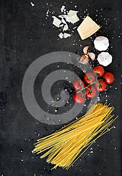 Food frame. Pasta ingredients. Cherry-tomatoes, spaghetti pasta, garlic, basil, parmesan and spices on dark grunge