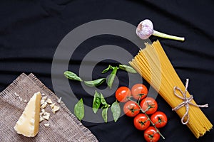 Food frame. Pasta ingredients. Cherry-tomatoes, spaghetti pasta, garlic, basil, parmesan and spices on dark background, copy