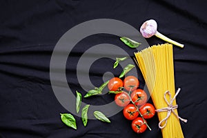 Food frame. Pasta ingredients. Cherry-tomatoes, spaghetti pasta, garlic, basil, parmesan and spices on dark background, copy